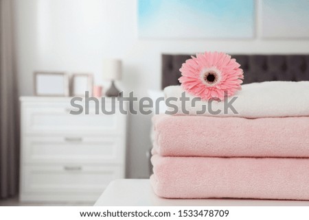 Stack of clean towels with flower on table in bedroom. Space for text