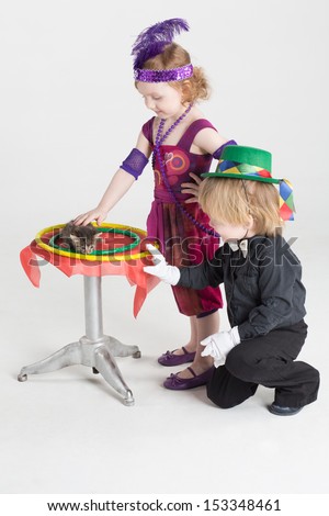 Little girl and boy in costumes of magicians next to the small round table with a kitten and rings