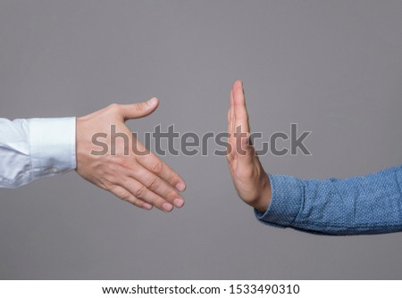 Businessman hands one with handshake, the other gesturing stop sign, gray background.