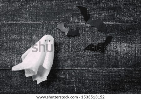 White ghost costume on dark black wooden background. Minimalistic Halloween concept. craft paper ghosts
