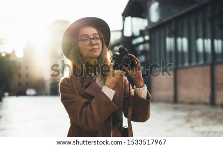 Photographer in glasses with retro camera take photo in city. Tourist smiling girl in hat travels in Barcelona holiday. Sunlight flare street in europe. Traveler hipster shoot sun day