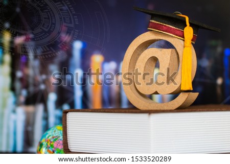 Education world knowledge ideas. Graduation cap, wood email address symbol on textbook, blur HUD graphic city network background. Concept of success business study abroad educational