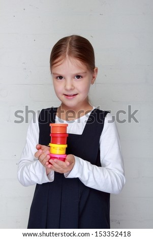 Happy little girl in school uniform holding a tube of paint for painting on Education
