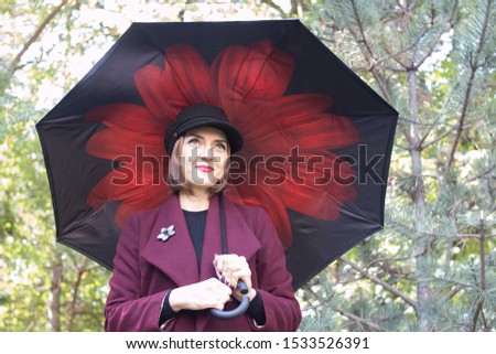 A young girl at the age of 33 years. In a Burgundy coat. In a black cap. With a big black umbrella. On the background of trees and spruce.
