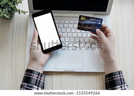 top view of a woman's hand has a credit card and a smartphone on a white blank screen. Concept of using credit cards