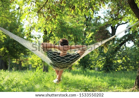 Young man resting in comfortable hammock at green garden Royalty-Free Stock Photo #1533550202