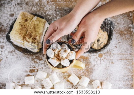 Hands holding cup with marshmallows near sweets plate