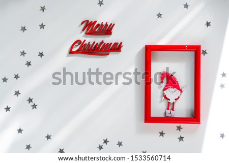 Funny handmade red gnom on frame with silver stars and letter Merry Christmas on white christmas background for a greeting card. Copy space flat lay