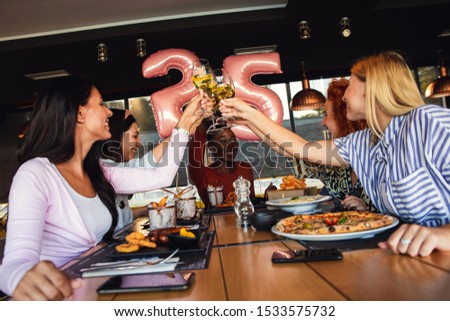 Group of young female friends having fun in restaurant, toasting with wine talking and laughing while dining at table.