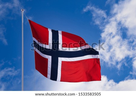 Norwegian flag on a pole moving in the wind. Sunny weather with blue sky and some clouds in the background.