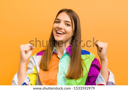 young pretty woman feeling happy, positive and successful, celebrating victory, achievements or good luck isolated against flat background