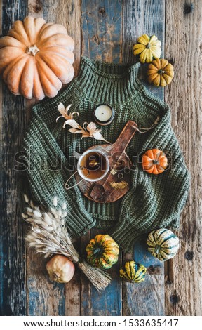 Autumn outfit layout. Flat-lay of dark green knitted sweater, blue jeans, hat, decorative pumpkins, candle, accessories and tea in cup on board over wooden background, top view. Fall apparel and mood Royalty-Free Stock Photo #1533635447