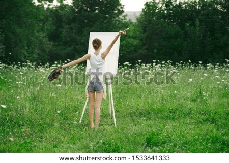 young woman in nature draws a picture on canvas