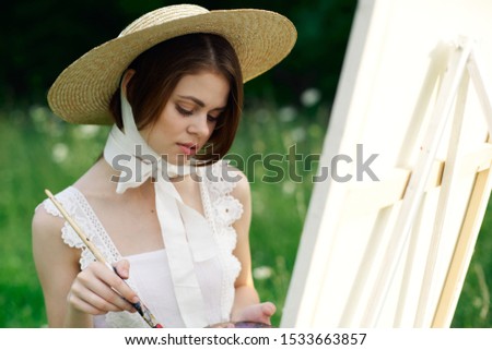 young woman in hat paints a beautiful model paints a picture