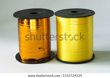 Golden and yellow shiny floristic ribbon in a bobbin on a white background with shadow. Art materials for gifts and flowers bouquets packaging. Accessories for hand-made and sewing shops. Copy space.