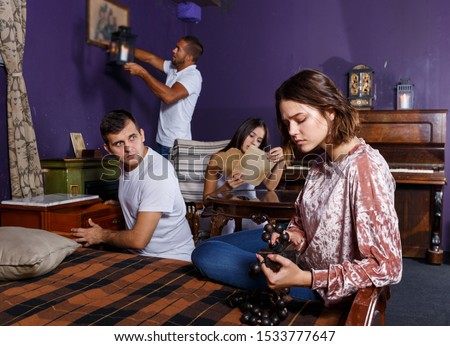 Young people looking at old wooden rosary while pursuing investigation in escape room with antique furniture Royalty-Free Stock Photo #1533777647
