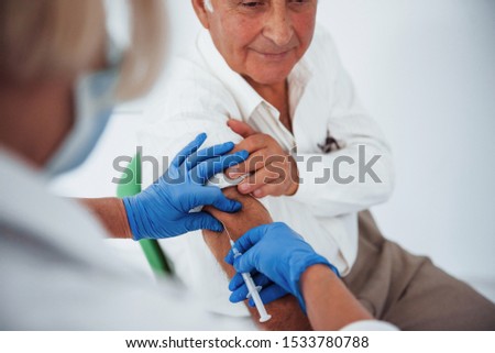 Female doctor injecting senior male patient with syringe in the clinic.