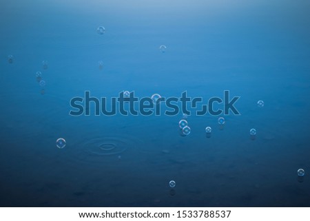 Soap bubbles flying and floating on a calm blue lake water surface.