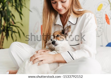 Image of a cheery young cute girl in pajama at home on bed with her dog cuddling.