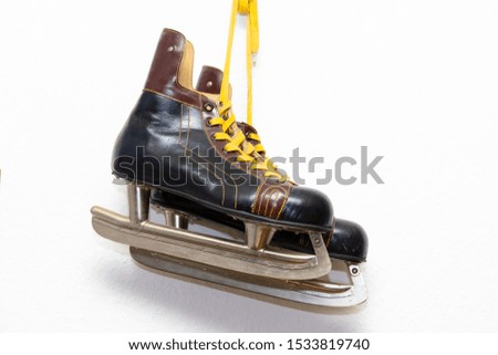 A pair of brown worn skates with yellow leather laces on shiny metal runners against white background. These shoes are several decades old but still in good condition.