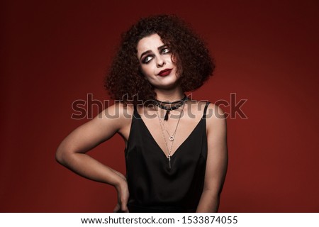 Image of displeased witch girl in black dress with halloween makeup looking aside isolated over red wall