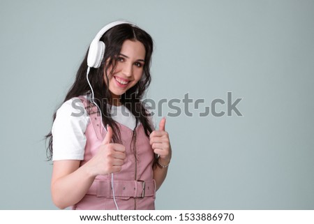 Awesome brunette lady in pink leather dress listen for her favourite music with white headphones. Audio book or internet radio podcast broadcast listen. enjoy and relax music. Thumb up gesture