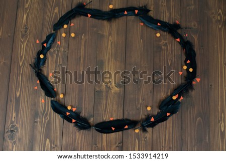 Flat lay shot  of a black feather that is lined up in a circle with candy and orange paper on a wooden table.