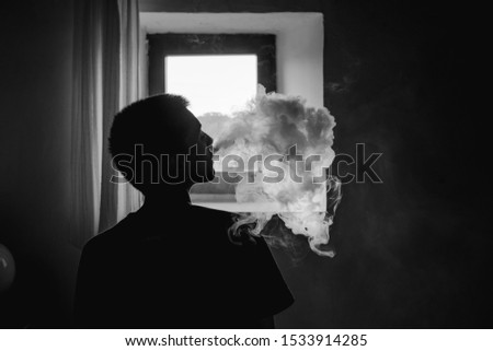 Stock photo of black and white photo of a silhouette of a person smoking through the nose in front of a window