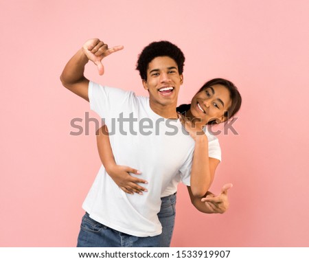 Cute couple hugging, making frame with hands and taking picture over pink background