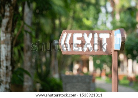 exit sign on a wooden plank, old, vintage, left direction sign, against the background of green trees in the hotel