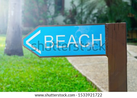 signpost beach, made of wood, green, the road to the beach to the left, on the background of the road and the green plants of the hotel