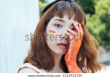 Close up shot of a artist girl's head with orange left hand cover her left face.