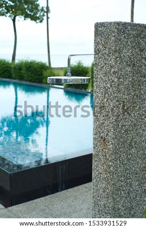 Stainless shower on the stone column with blue sky and swimming pool in background