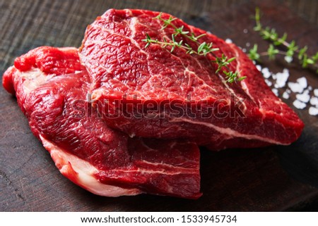 Boneless top chuck steak - beef cuts on a rustic wooden cutting board on a dark wooden table with fresh thyme on top and sea salt, close-up Royalty-Free Stock Photo #1533945734