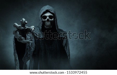 Grim reaper reaching towards the camera over dark background with copy space Royalty-Free Stock Photo #1533972455