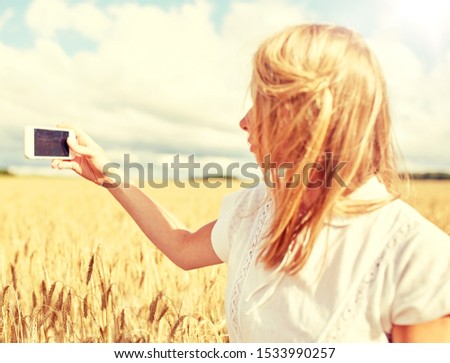 nature, summer vacation, technology and people concept - close up of young woman with smartphone taking picture of cereal field