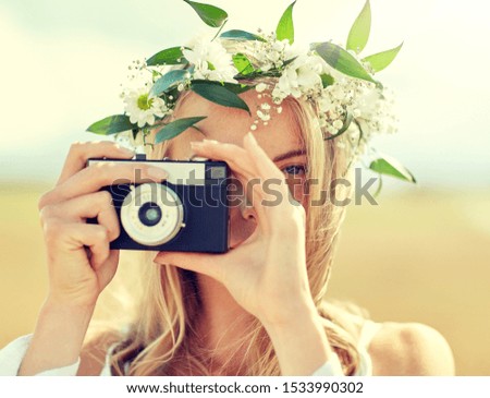 nature, summer holidays, vacation and people concept - close up of happy woman in wreath of flowers taking picture with film camera outdoors