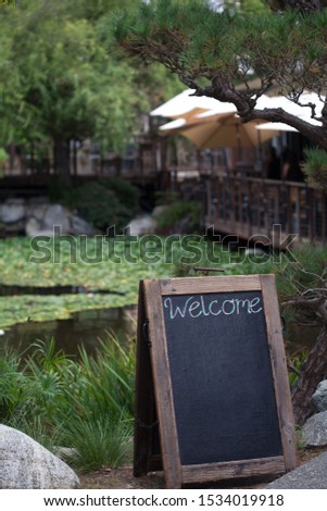 Blackboard with chalk written sign at the entrance to the restaurant with water lilies pond