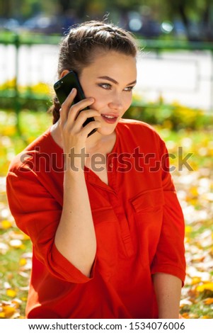 Portrait of a young beautiful brunette calling by smart phone on a background of autumn street