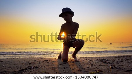 Young boy with hat collecting peebles on beach and throw stone skipping game on sea sunset water surface, small flattened rock bouncing off water surface across body of water many times