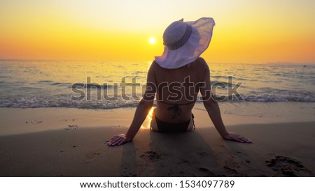 Young woman in big hat relaxing on beach at sunset. Travel and summer concept