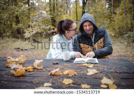 Handsome loving couple sitting on the bench in the autumn park reading a book, having fun together. Love and tenderness. Relationships, friendships, education, lifestyle concept