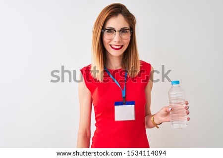 Redhead businesswoman wearing id card drinking water over isolated white background with a happy face standing and smiling with a confident smile showing teeth