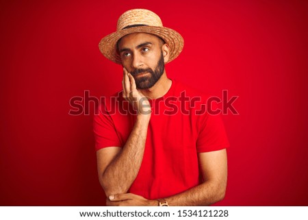 Young handsome indian man wearing t-shirt and hat over isolated red background thinking looking tired and bored with depression problems with crossed arms.