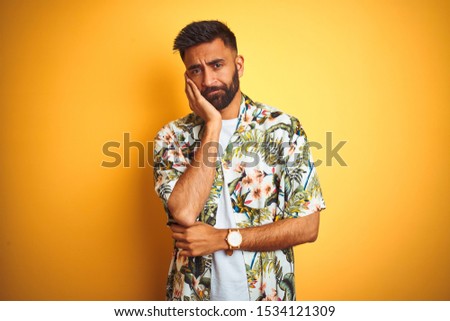 Young indian man on vacation wearing summer floral shirt over isolated yellow background thinking looking tired and bored with depression problems with crossed arms.