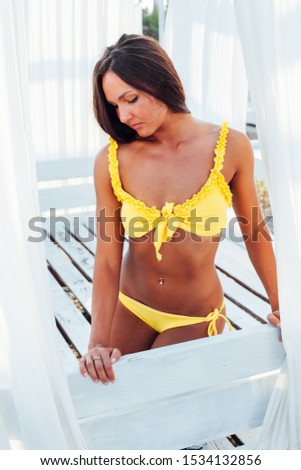 slender woman in yellow swimsuit sunbathes on the beach by the sea