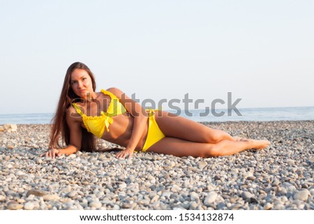Beautiful slender woman in yellow swimsuit sunbathes on the beach by the ocean