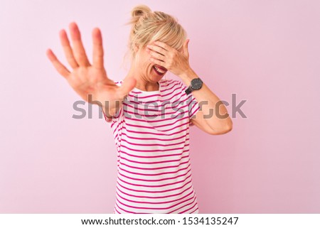 Middle age woman wearing striped t-shirt standing over isolated pink background covering eyes with hands and doing stop gesture with sad and fear expression. Embarrassed and negative concept.