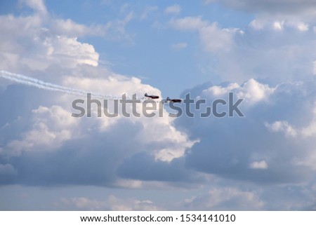 Colorful photo of two passenger stunt planes moving dynamically across the sky and flying from left to right while generating some smoke behind them seen on a cloudy summer sky in Poland