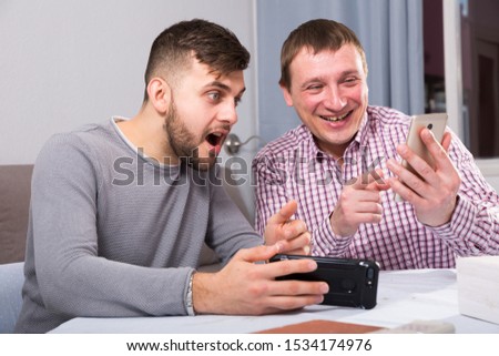 Friendly male meeting over beer at home, men looking at phone and discussing